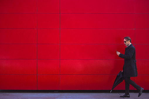 Handsome man in black walking beside the red wall