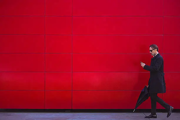 Photo of Handsome man in black walking beside the red wall