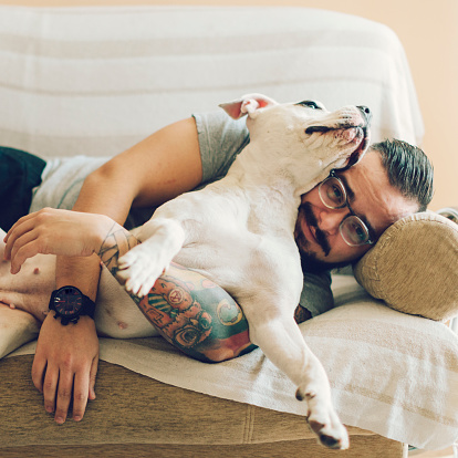 Man with tattoos and beard embracing his dog, staffordshire terrier, female animal 18 months old. Looking at camera and smiling.