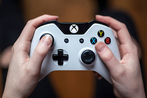 White Xbox One Controller - Close Up Gothenburg, Sweden - January 17, 2015: A close up shot from above of a young woman's hands holding a white Xbox One controller as she is playing a video game. Natural lighting, shot on wooden background with shallow depth of field. brand name games console stock pictures, royalty-free photos & images