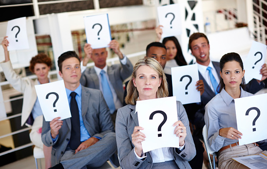 Shot of a group of businesspeople holding up signs with question marks on them during a work presentation