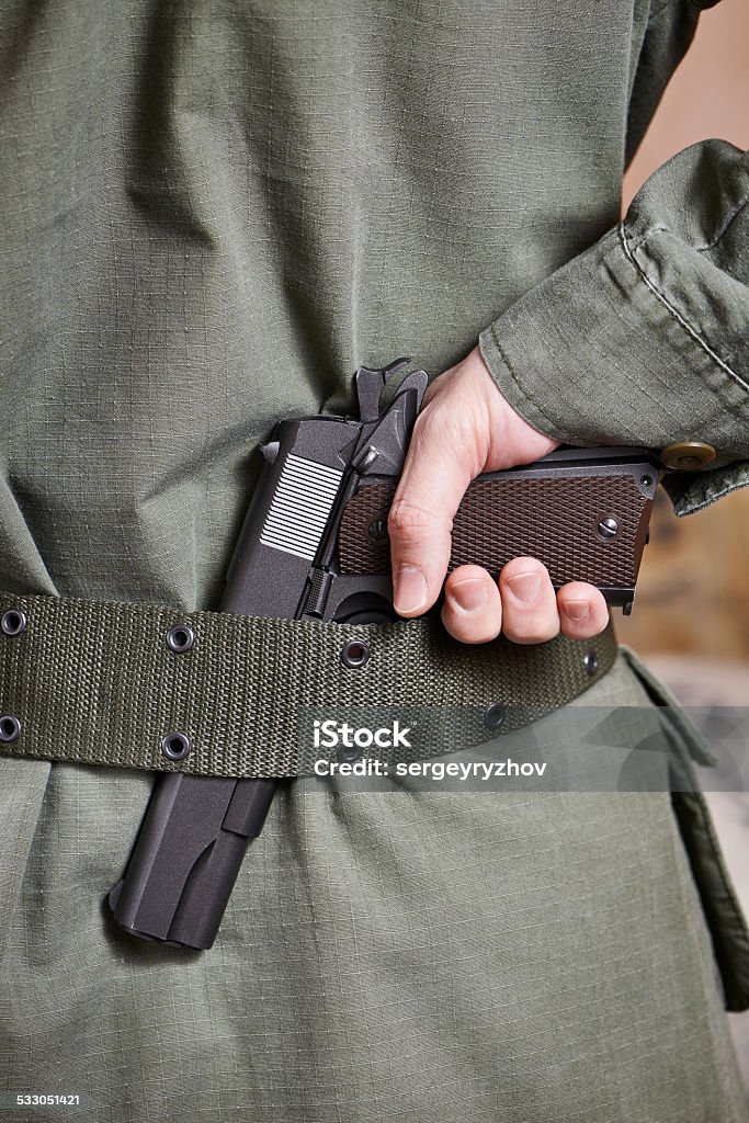 Soldier in uniform holding gun in his belt Soldier in uniform holding a gun in his belt 2015 Stock Photo