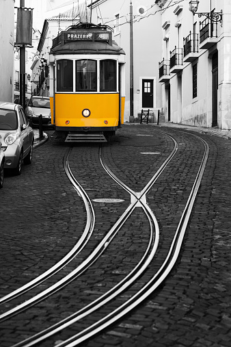 Old-fashioned yellow tram (line 28) moving through the old town district of Alfama in Lisbon.