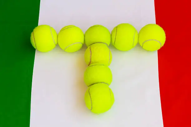 a set of balls forming the letter T yellow to practice the sport of tennis, in the background with the italian flag with the colors red,green and white