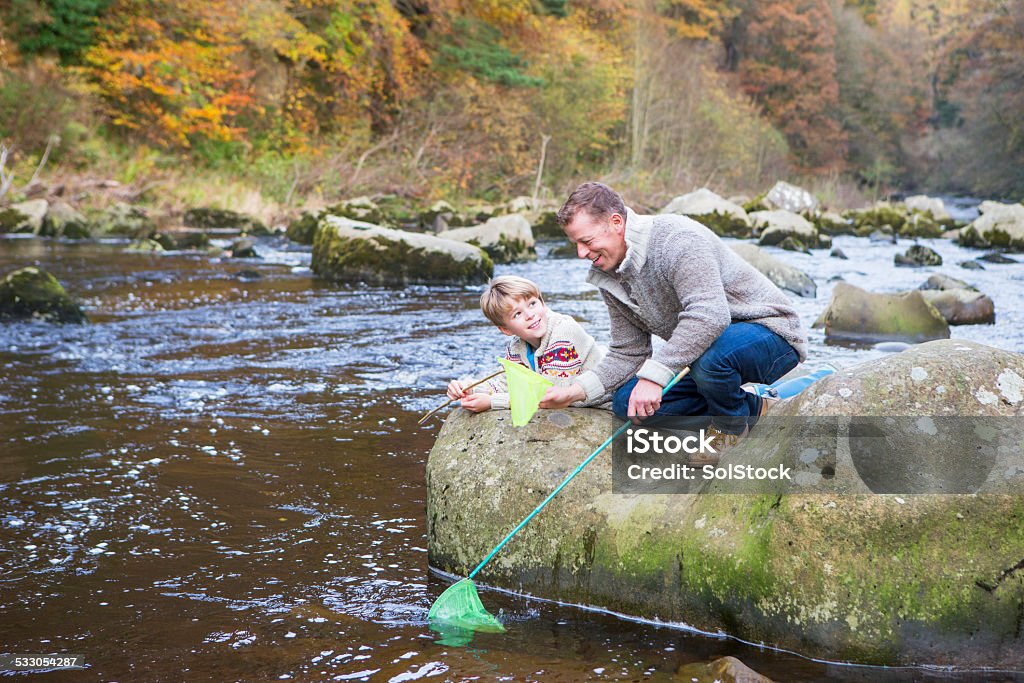 Father and Son Fishing A happy father and son lie on a rock as they fish by the river with nets. 2015 Stock Photo