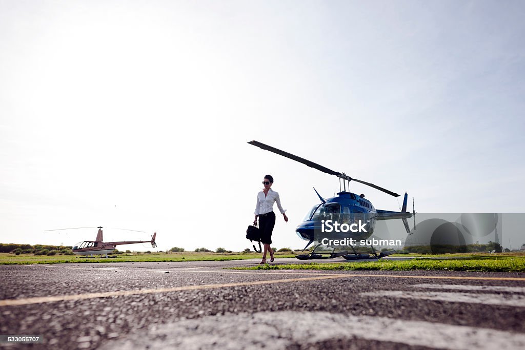 Confident & Successful Businesswoman carrying her briefcase walking on helipad away from the helicopter. Helipad Stock Photo