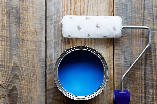painting with  can of blue paint and roller top view on wooden background