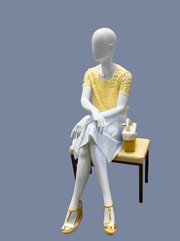 Sitting female mannequin dressed with fashionable modern clothes, against gray background. No brand names or copyright objects.