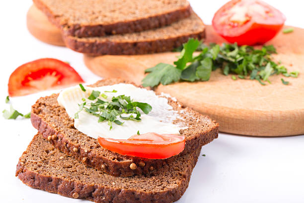 Sandwiches from rye bread on a white background. Oil, tomatoes, greens on a wooden kitchen board. Close up, small depth of sharpness