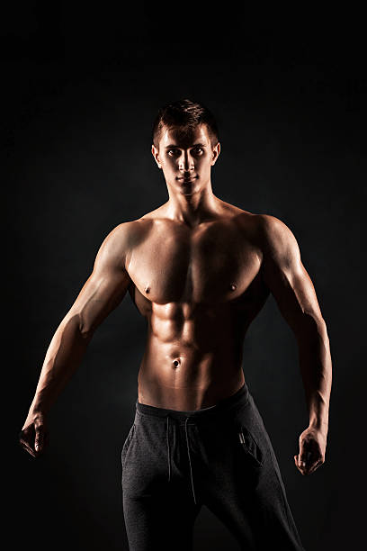 istock Sexy shirtless bodybuilder posing, looking at camera on black ba 533062034