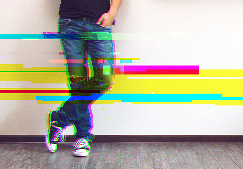 Glitched style photo of young fashion man's legs in jeans and sneakers on wooden floor
