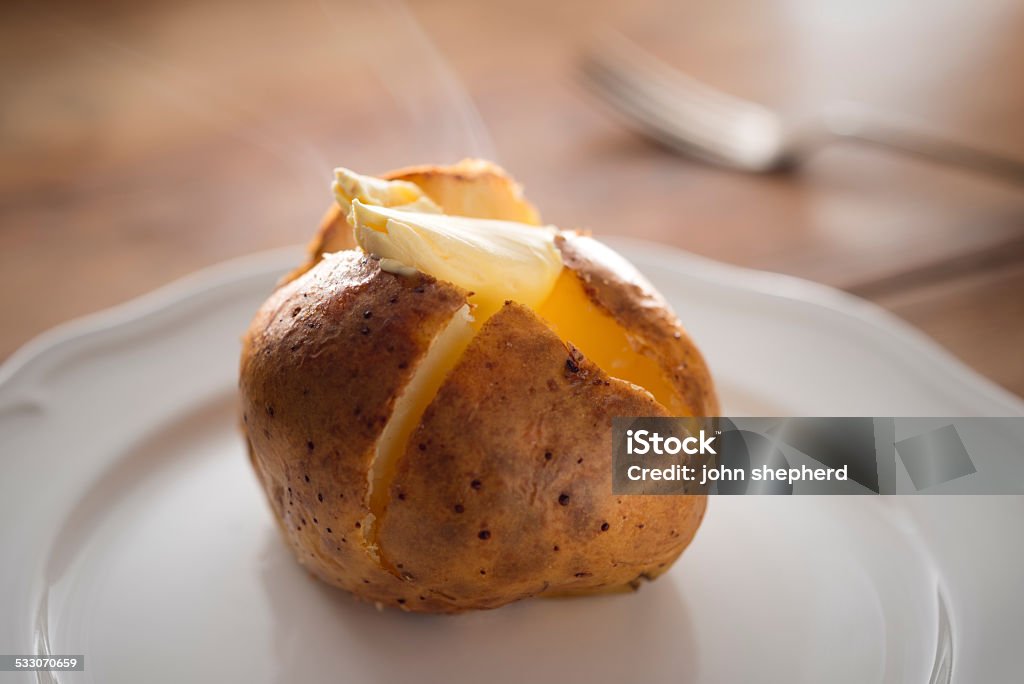 Steaming hot Baked Potato with melting butter. Steaming hot Baked Potato, sliced open filled with melting butter with steam flowing. Baked Potato Stock Photo