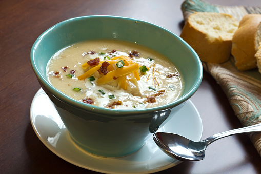 Creamy loaded baked potato soup with scallion garnished and fresh Italian bread