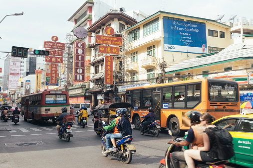 On an overcast day Yaowarat Road in Chinatown is bustling with traffic. Numerous signs hang above. Buses, taxis, tuk tuks, and hired motorbikes drive along the well known street. Photographed with a Nikon D800 on an overcast day.