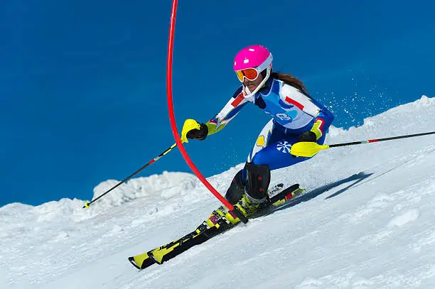 Side view of young female skier touching the red pole during the slalom ski race