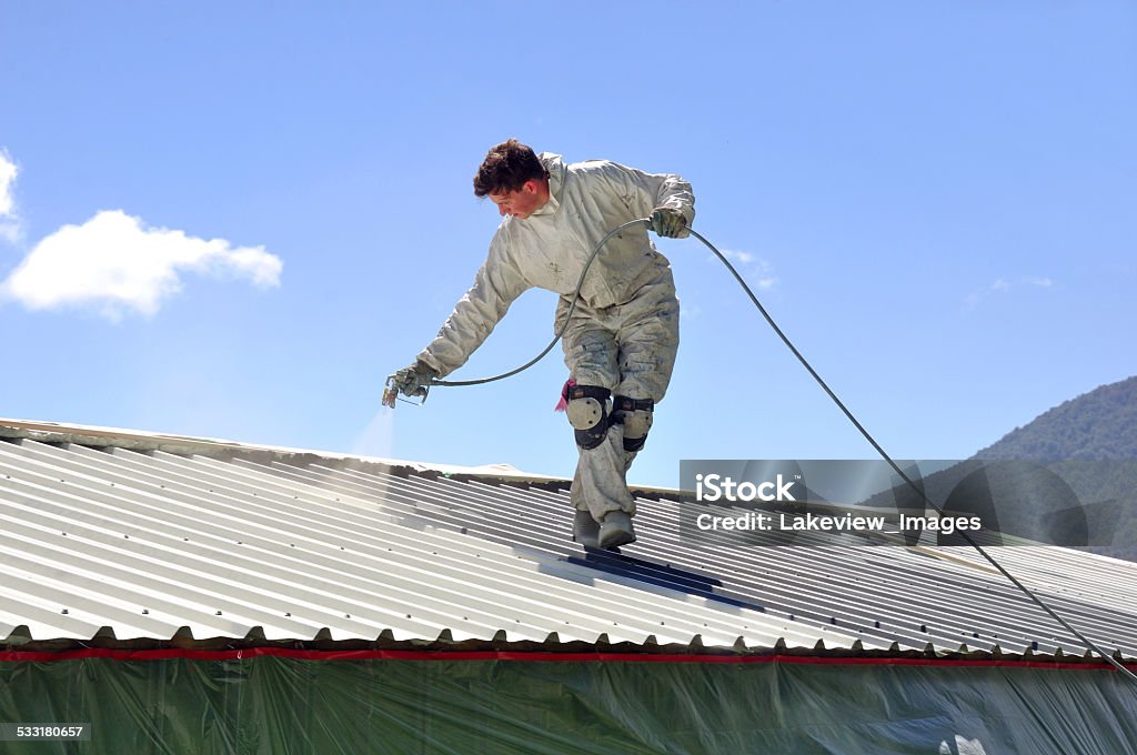 painting the roof A trademan uses an airless spray to paint the roof of a building Rooftop Stock Photo