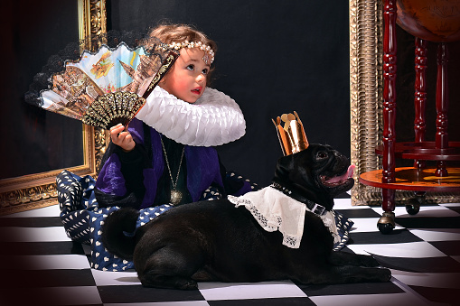 Beautiful little princess  with a fan and a  coronated dog.