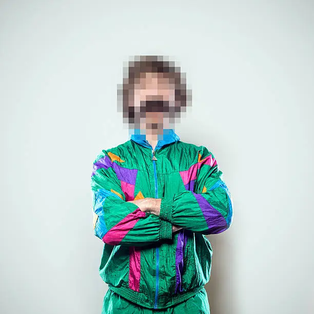 A portrait of a man in a track suit with a mustache from the waist up, whose face has been rendered unrecognizable by being pixelated.  A conceptual representation of individual identity protection.  Square crop with copy space on a a clean off-white background.