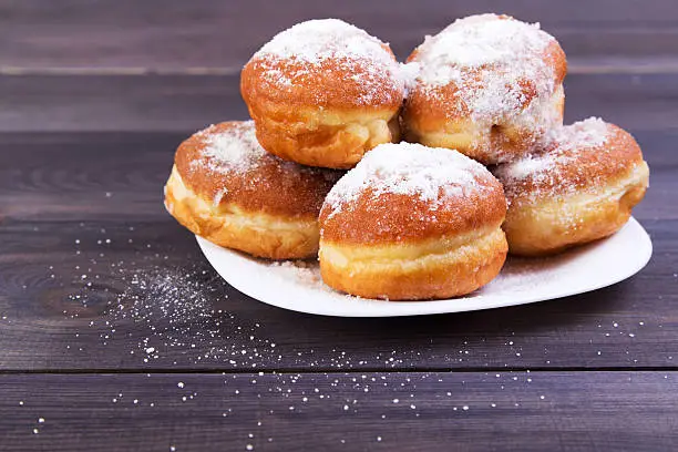 German donuts - berliner with icing sugar on plate on a dark wooden background