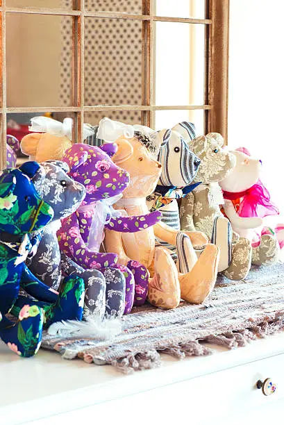 Many tilda textile teddy bear toys sitting in a row in workshop. Indoors.