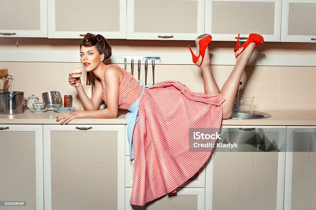 The girl on the kitchen table. Girl in red shoes climbed on the kitchen table and eat cake. Bizarre Stock Photo