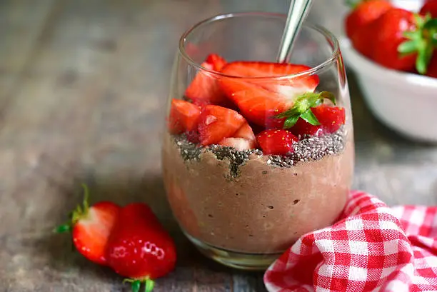 Chocolate chia seed pudding with strawberry in a glass on a rustic wooden table.