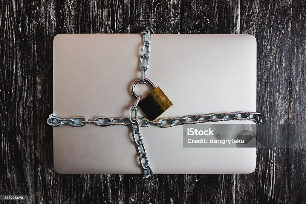 Heavy with a padlock around a laptop isolated Heavy with a padlock around a laptop isolated on grey table. Bathroom Stock Photo