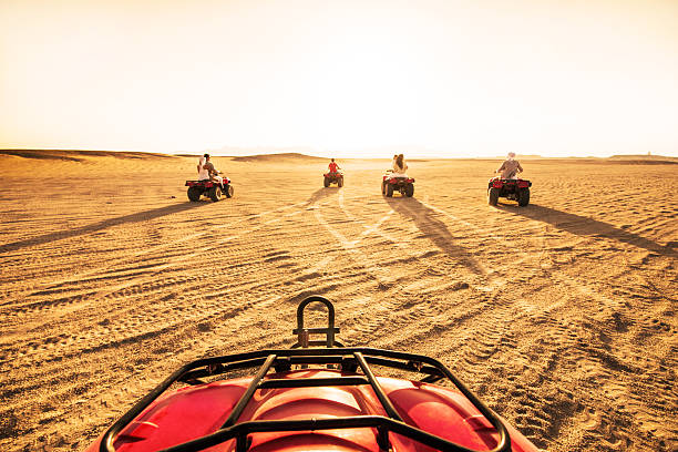 Group of people people driving quad bikes. Rear view of group of people having fun while driving quad bikes in the desert at sunset. Copy space. dirt road sunset stock pictures, royalty-free photos & images