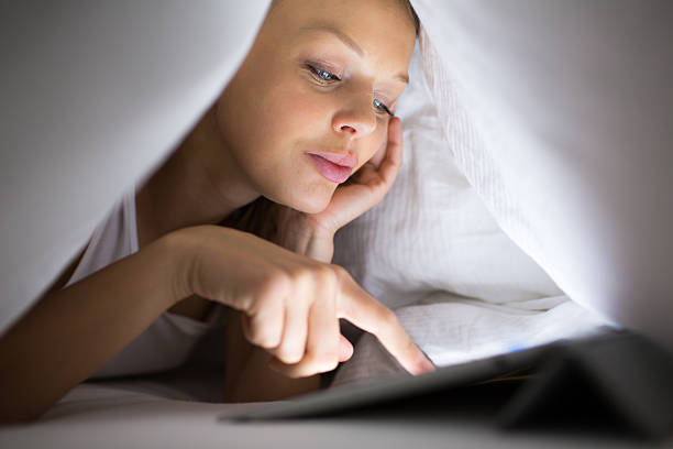 Pretty young woman watching on her laptop Pretty, young woman using her tablet computer in bed late at night, being online, browsing through the internet, reading news, staying in touch with friends, shopping online ugly people crying stock pictures, royalty-free photos & images