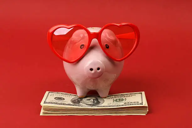 Photo of Piggy bank with heart sunglasses standing on stack of money