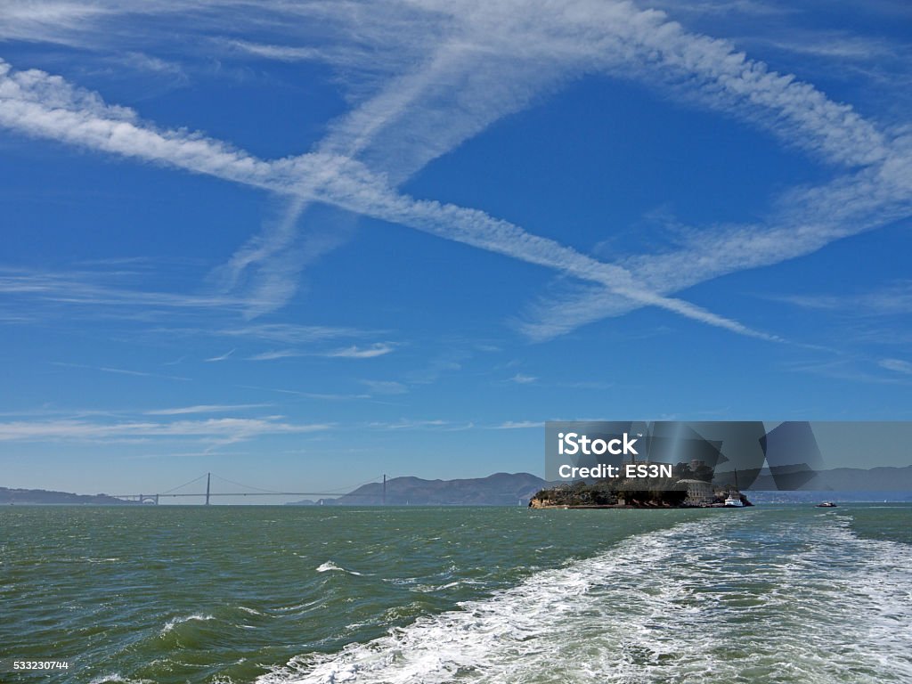 Alcatraz and Golden Gate Alcatraz prison Island from the water, boat wake, bay view, dramatic sky with vapour trails, Golden Gate bridge in background Alcatraz Island Stock Photo