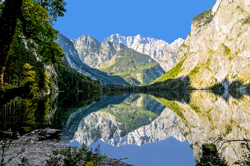 Beautiful scenery in the Alps. On a bright day, with clear blue sky, the mountains reflect in the mirror-like lake surface. Horizontal orientation.