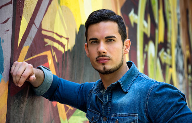 Serious young man leaning on colorful graffiti wall