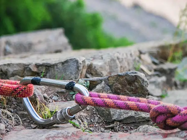 Steel carabine hook with a climbing-rope on rock background. Closeup.