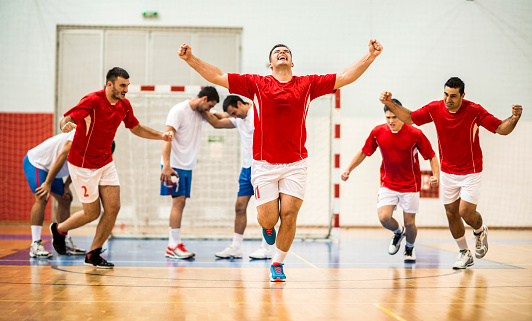 Young handball player celebrating his goal, while other players are in the background.   