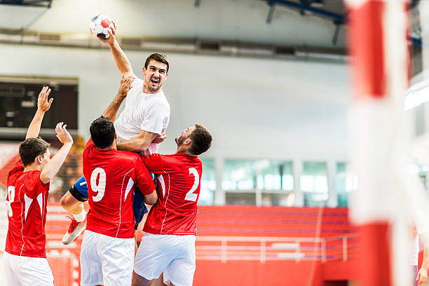 Handball player shooting at goal. Young handball player is shooting at a goal, while his opponents are holding him.    handball stock pictures, royalty-free photos & images