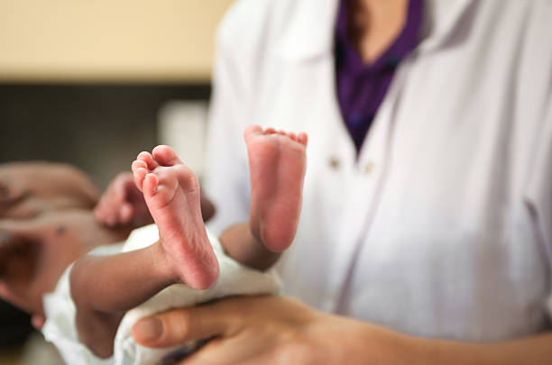 Doctor is holding tiny baby, feet are visible. Doctor or nurse is holding a baby. Baby's feet are most in focus. Baby is malnourished and tiny. Baby is wearing a diaper. senegal photos stock pictures, royalty-free photos & images
