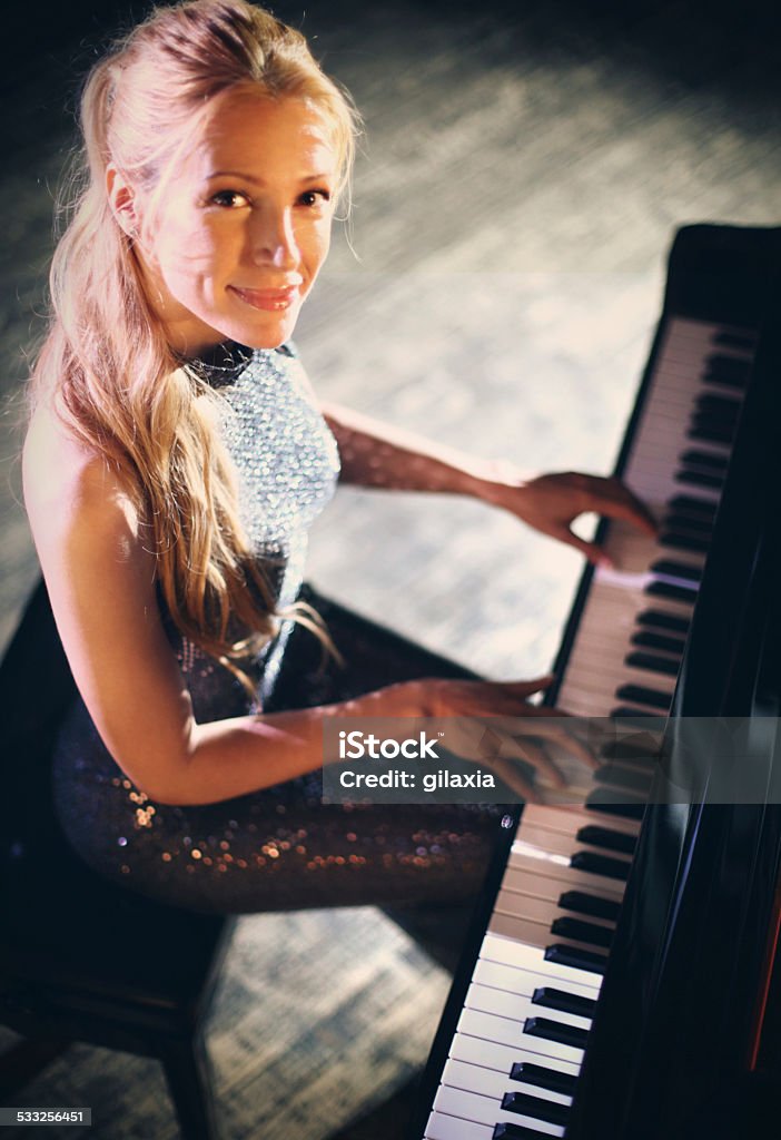 Pianist woman at concert. Smiling mid aged female pianist sitting by piano. Wearing long elegant dress and hair pulled back. Looking at camera and smiling. 2015 Stock Photo