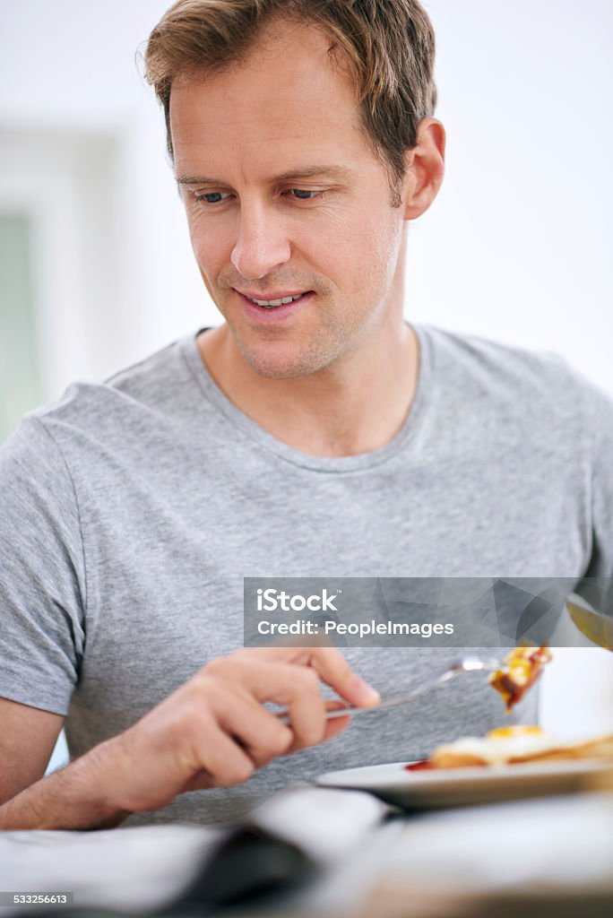 That's interesting... Shot of a handsome man reading the paper while eating breakfast 2015 Stock Photo