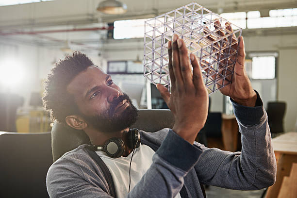 Hmmm... Shot of a young male designer looking thoughtfully at the cube model he's holding new idea office stock pictures, royalty-free photos & images