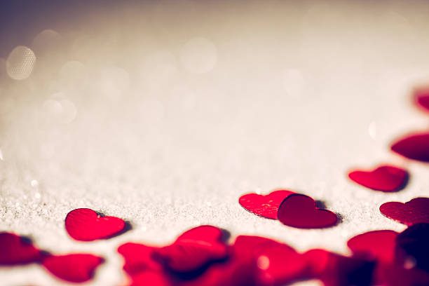Macro photography of glitter hearts on red defocused background.
