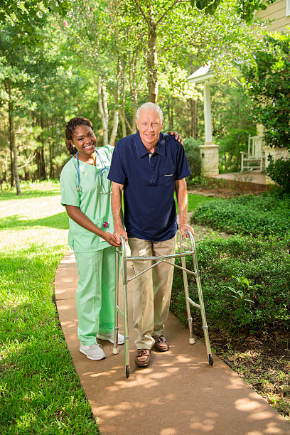 opieki zdrowotnej: pielęgniarka pomaga starszy człowiek na zewnątrz za pomocą walker. dom opieki. - nursing home senior adult home caregiver physical therapy zdjęcia i obrazy z banku zdjęć