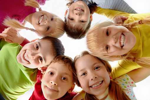 A small group of Elementary students huddle together with their heads in a circle as they pose for a portrait.  They are each dressed casually and smiling as they look down to the camera.