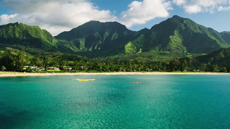 Aerial view flying over hawaiian canoes towards beautiful green mountains and