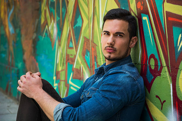 istock Serious young man sitting against colorful graffiti wall 533278425