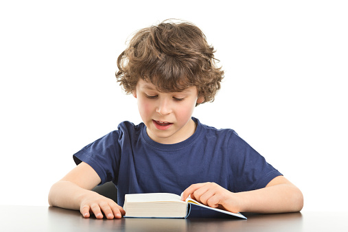 7 years old boy in tshirt reading book isolated on white