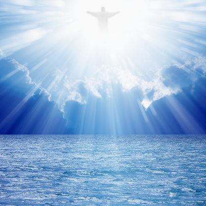 Christ silhouette in blues skies over sea, bright light from heaven