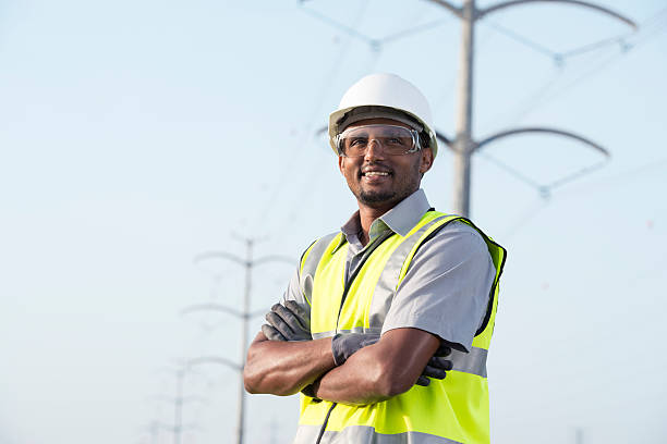 Portrait of manual worker / electrician / lineman / engineer / technician. Portrait of manual worker in Personal protective equipment (PPE) standing under high voltage transmission lines against tubular transmission towers. ethiopian ethnicity photos stock pictures, royalty-free photos & images