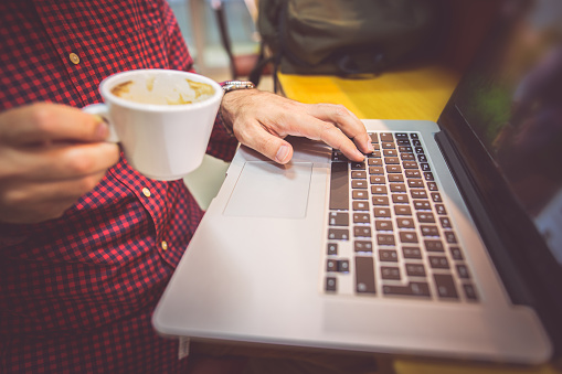 Photo of man typing on laptop and holding a cup of coffee in the coffee shop