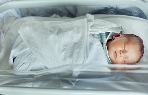 Newborn baby boy asleep in hospital bassinet